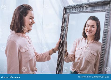 Beautiful Smiling Young Woman Standing Near Mirror And Looking Stock