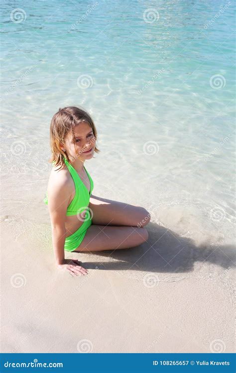 junges mädchen in einem kalk farbigen badeanzug der auf dem strand durch das wasser sitzt