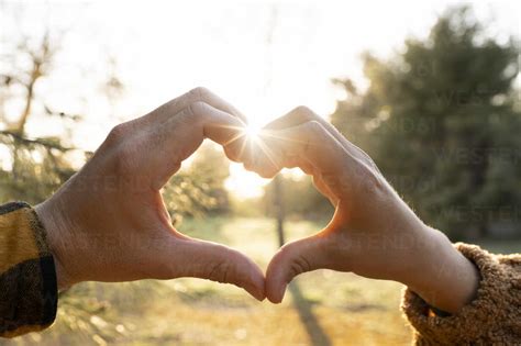 Man And Womans Hands Making Heart Shape Symbol During Sunset Stock Photo
