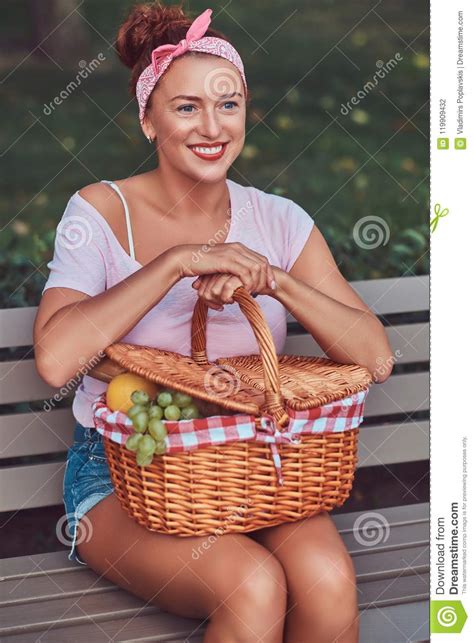happy beautiful redhead female wearing casual clothes holds a picnic basket while sitting on a
