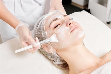 Premium Photo Cosmetologist Applies Cream Mask On Woman Face For Rejuvenation Face Skin