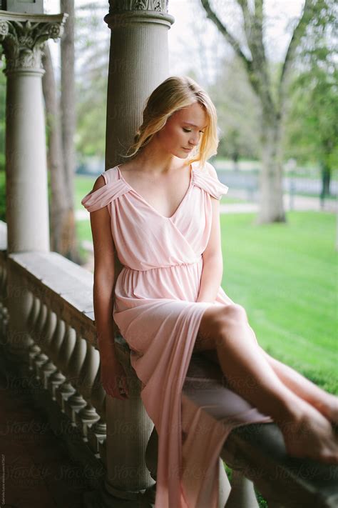Beautiful Girl In Pink Grecian Gown Sitting On An Stone Balcony By