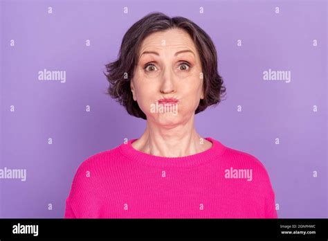 portrait of attractive funny mature woman holding air in cheeks fooling isolated over violet