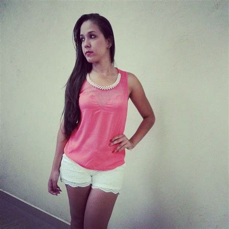 A Woman Standing In Front Of A Wall Wearing White Shorts And A Pink Tank Top
