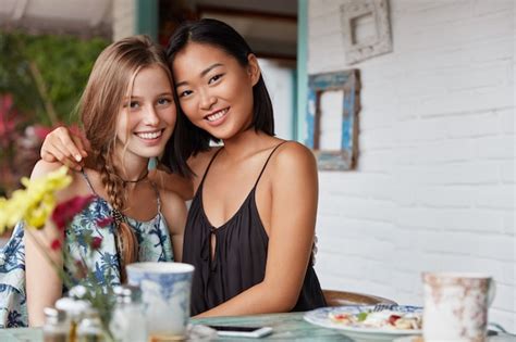 異人種間の真の友情や関係を示すさまざまな国籍の美しい若い女性が混血の人種を受け入れ、バーでコーヒーを飲む 無料の写真