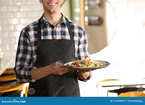 Young Waiter In Uniform Holding Tray With Tasty Dish Stock Photo