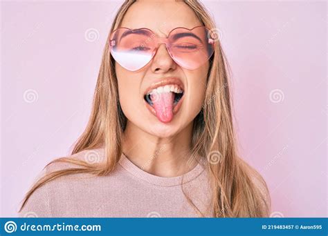 Young Beautiful Blonde Woman Wearing Heart Shaped Sunglasses Sticking Tongue Out Happy With