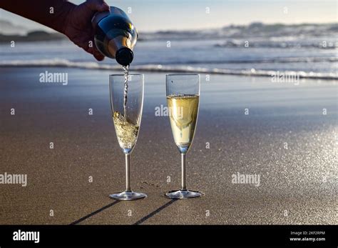 pouring of cava or champagne sparkling white wine on white sandy ocean beach on sunset in