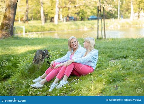 Mom And Daughter Siting On Green Grass In Park And Laugh Blondes Have Good Time Together In