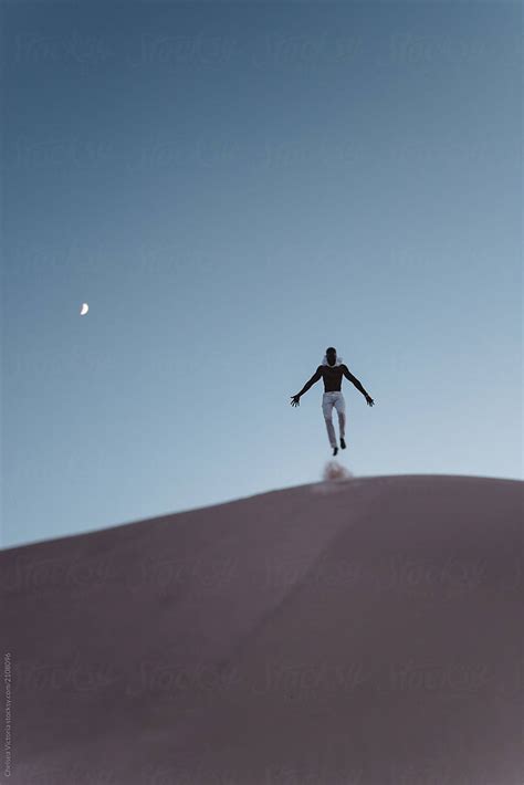 A Young Black Man Jumping In Dunes Of Sand At Night By Stocksy