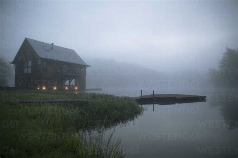 Log Cabin At Lakeshore During Foggy Weather Stock Photo