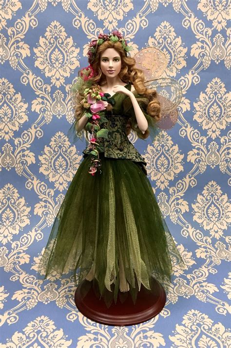 A Doll Is Dressed Up As A Fairy With Flowers In Her Hair And Green Dress