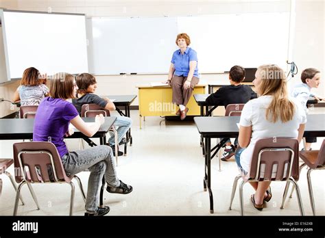 Teacher Sitting On Her Desk Teaching A Class Of Teenage Students Stock