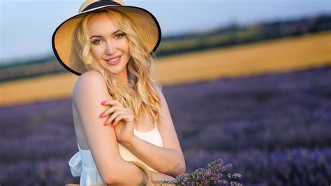 blonde beautiful smiley girl model is wearing white dress standing in blur lavender flowers
