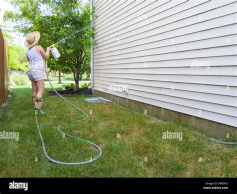 Woman Hosing Down The Sides Of Her House With A Handheld Pressure