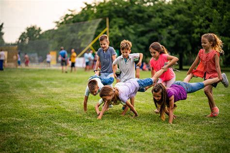 Group Of Children Playing Wheelbarrow Race In Park Stock Photo