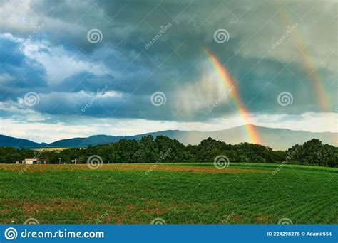 Two Rainbows Over A Field With A Storm In The Background Stock Photo