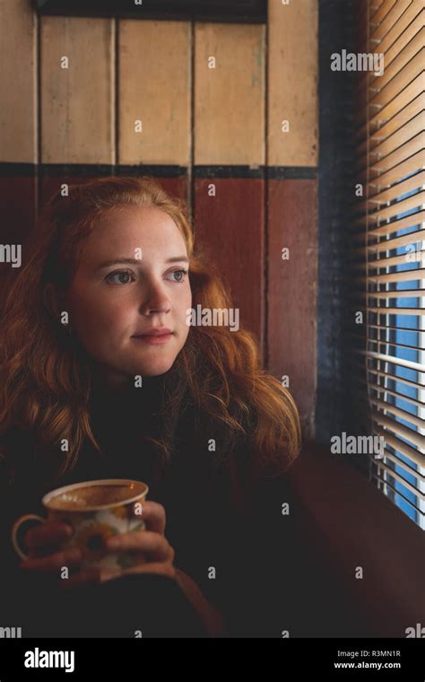 Redhead Woman Looking Through Window Blind In Cafe Stock Photo Alamy