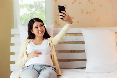 Happy Pregnant Asian Woman Taking Selfie On Smartphone In Bed At Home