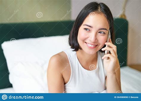 smiling korean girl in bed talks on mobile phone making a phone call lazy morning as asian