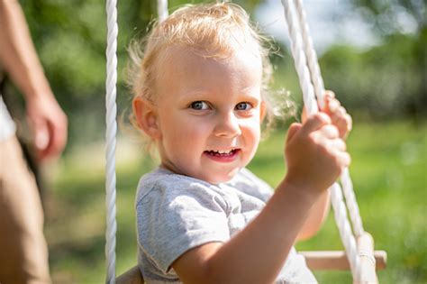 Happy Small Child Sitting In Baby Swing Outdoor In Backyard Stock Photo