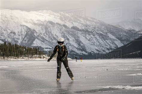 Woman Ice Skating On Frozen Lake Against Snowcapped Mountain Canadian