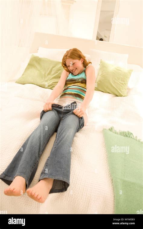 Teenage Girl 14 16 Sitting On Bed Putting On Jeans Stock Photo Alamy