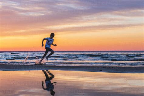 Boy Running On Beach At Sunset Stock Photo