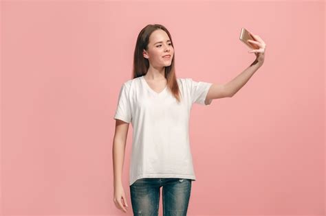 glückliches jugendlich mädchen stehend lächelnd auf rosa wand selfie foto per handy machend
