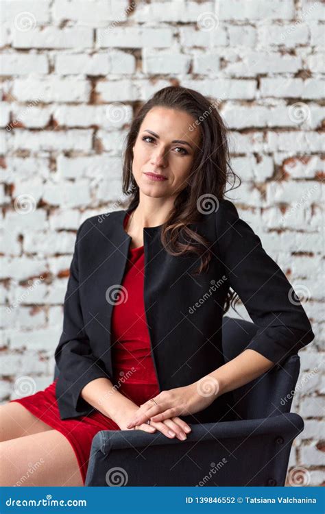 Portrait Of A Middle Aged Brunette Business Woman In A Short Red Dress And Black Jacket Sitting