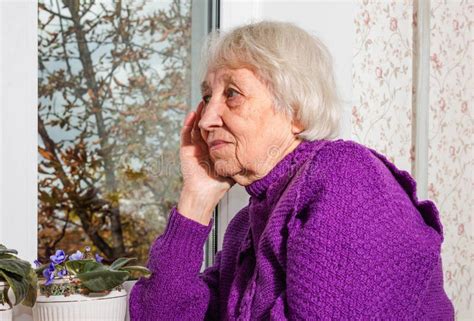 Old Lonely Woman Sitting Near The Window In His House Stock Image