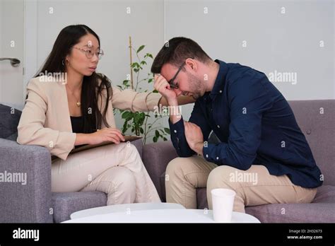 Asian Female Psychologist Comforting Her Caucasian Man Patient At