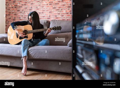 Woman Playing Guitar Sitting On Her Couch At Home And Learning With Online Lessons And Some