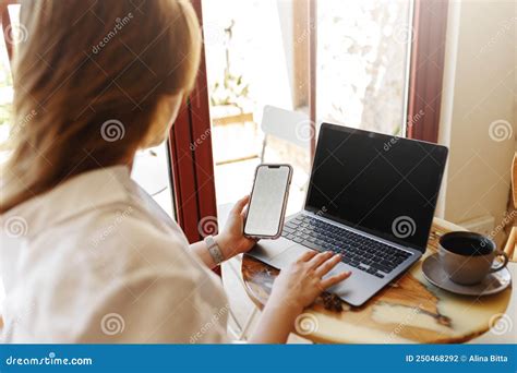 Back View Of Woman Watching Phone While Working On Laptop In Cafe Place Online Work Or