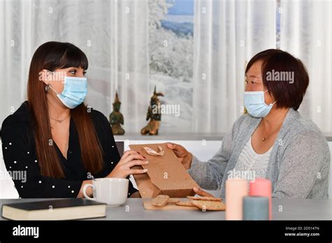 Young Woman Receiving A Paper T Bag From A Mature Asian Woman Both Using Face Masks On An