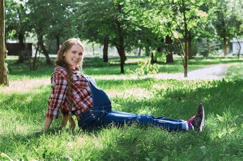 Premium Photo Beautiful Pregnant Woman In Denim Overalls Sitting On The Grass In The Park