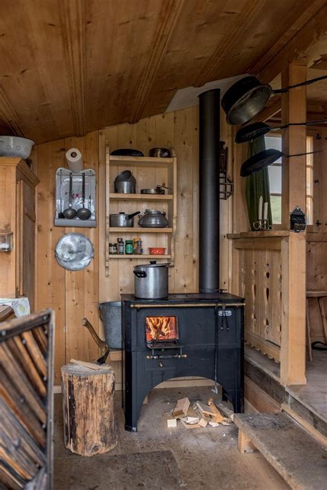 An Old Fashioned Stove In A Wood Cabin With Shelves And Pots On The Top