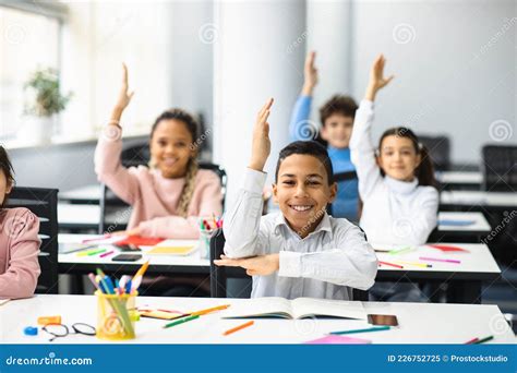 Happy Little School Children Raising Hands At Classroom Stock Image