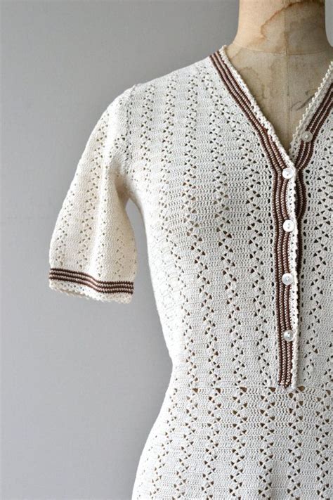 A White Crocheted Dress With Brown Trimmings On The Neck And Sleeves