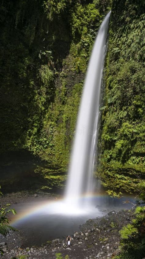 Vertical Shot Of A Thin Waterfall With A Beautiful Rainbow Flowing