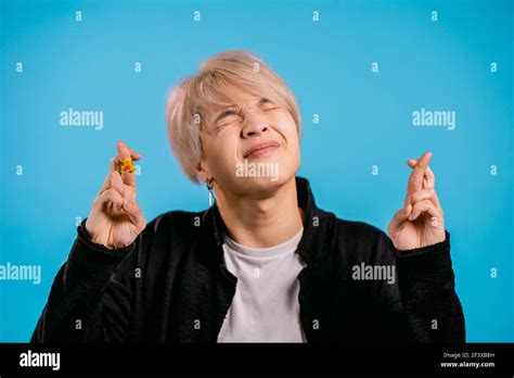 Handsome Asian Man Praying With Crossed Fingers Over Blue Background