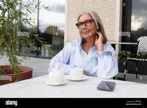 well groomed slender mature business woman with gray hair dressed in a shirt sits on the terrace