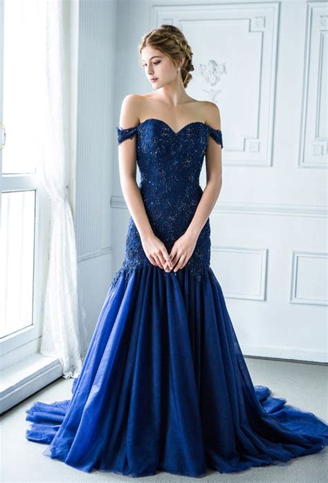 Style #481 is a beautifully delicate gown, with boning in the bodice, fun and full tulle skirt, and 3d floral appliqué on the shoulders. This off-the-shoulder midnight blue gown from Digio Bridal ...