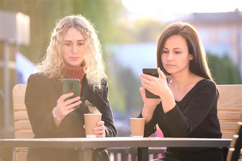 Premium Photo Two Distracted Female Friends Browsing Their Mobile Phones While Sitting