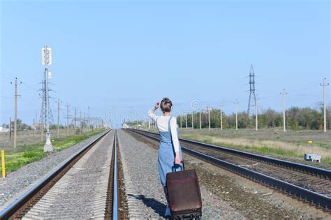Young Woman Walks With Suitcase Along The Rails Of Railway Back View