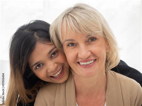 Portrait Of Asian Teen Daughter Is Hugging Her Adopted Caucasian Mother Looking At The Camera