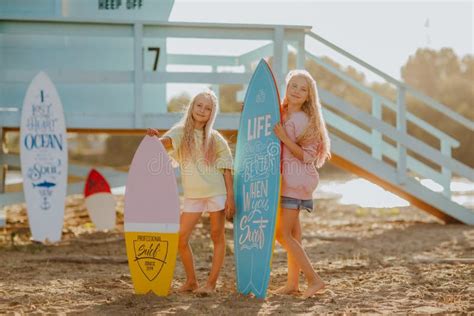Girls Posing With Surfboards Against Blue Lifeguard Tower On The Sand