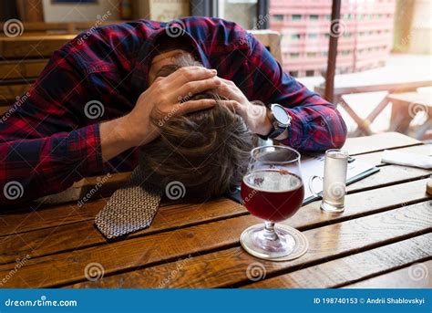 Upset Young Man Drinking Alcoholic Asleep At Table In Bar With Alcohol
