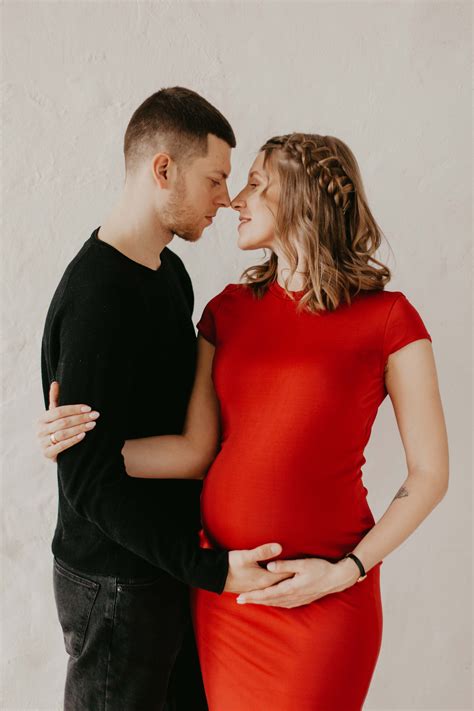 a pregnant woman in a red dress standing next to a man with his hand on her belly