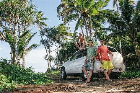 Three Young Happy Male Friends Next To A 4x4 Offroad Car On Exotic Tropical Island Full Of Palm